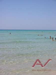 Mare azzurro trasparente con alcune persone che nuotano. Cielo sereno sullo sfondo.
