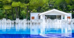 Piscina con sedie bianche e bar immerso nel verde.