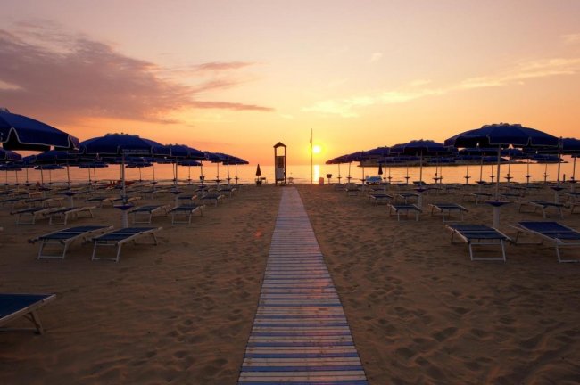 Spiaggia al tramonto con ombrelloni e lettini blu.