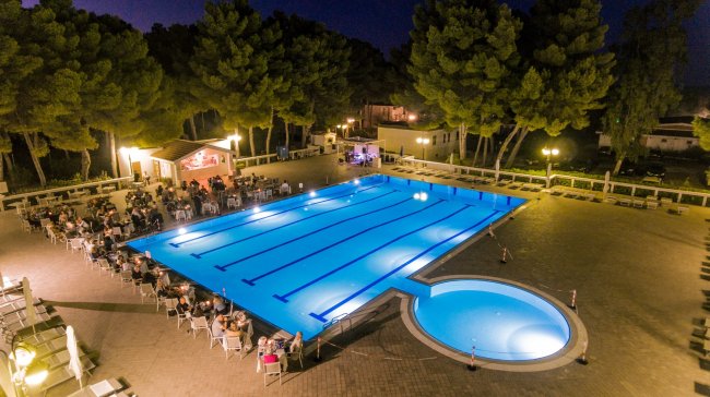 Piscina illuminata di notte con bar all'aperto.
