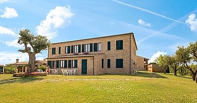 Grande casa in mattoni con giardino e alberi, cielo sereno.