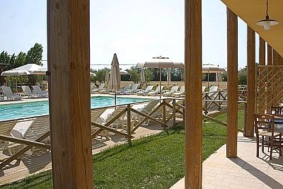 Piscina con lettini e ombrelloni, vista attraverso colonne in legno.