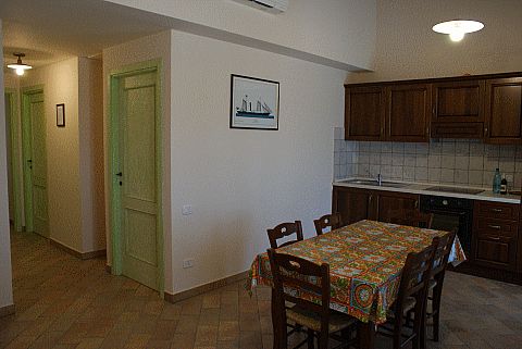 Cucina con tavolo, sedie, porte verdi e un quadro sul muro.