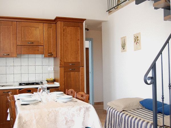 Cucina con mobili in legno, tavolo apparecchiato e una scala a chiocciola.