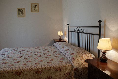 Letto matrimoniale con copriletto a fiori, comodini con lampade accese, decorazioni murali sopra.