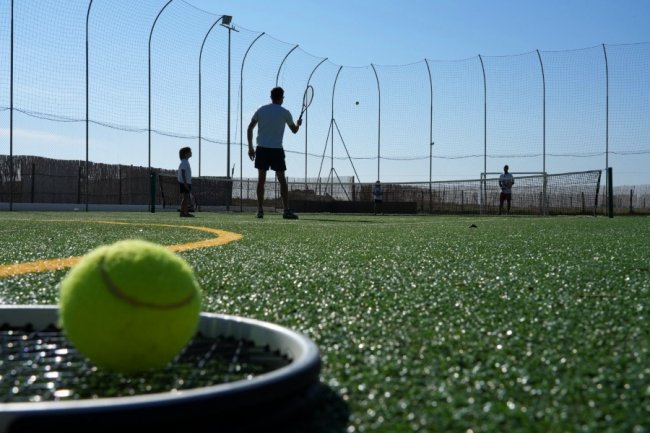 Persone giocano a tennis su un campo sintetico.