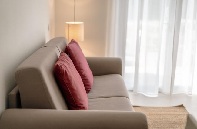 Divano beige con cuscini rossi e lampada accesa.