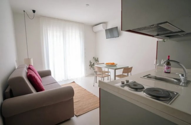 Soggiorno con divano beige, cucina e tavolo da pranzo.