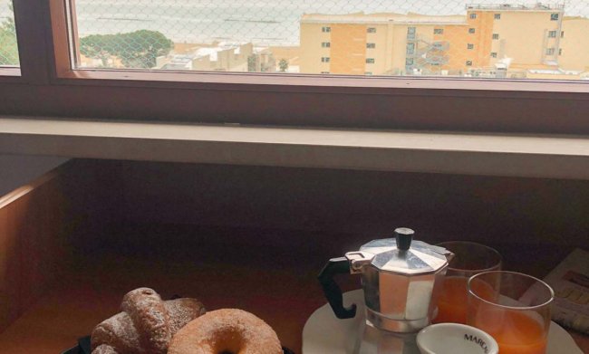 Colazione con vista su palazzi e mare dalla finestra.