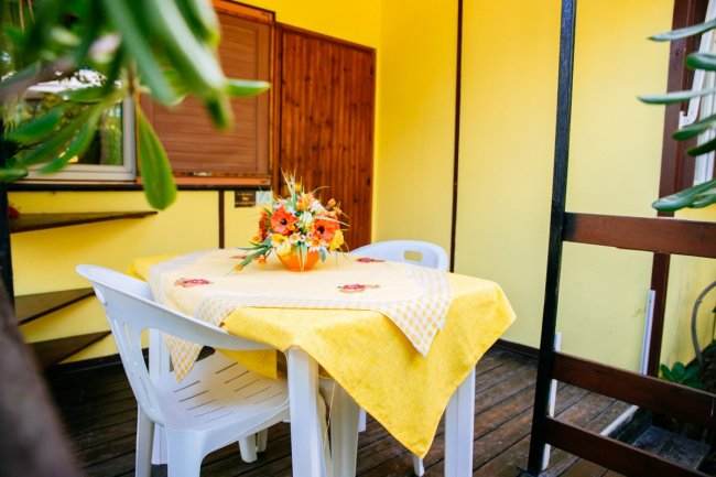 Tavolo da esterno con fiori e sedie bianche su una veranda gialla.