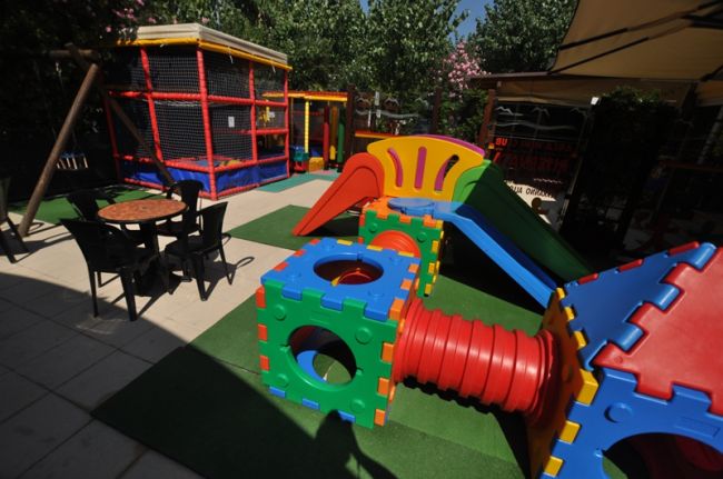 Parco giochi con scivolo colorato, tunnel e tavolino con sedie.