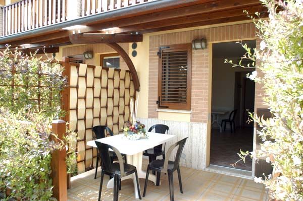 Terrazza esterna con tavolo e sedie nere, circondata da piante.