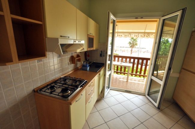 Una cucina con mobili chiari, piano cottura a gas e porta-finestra aperta sul balcone.