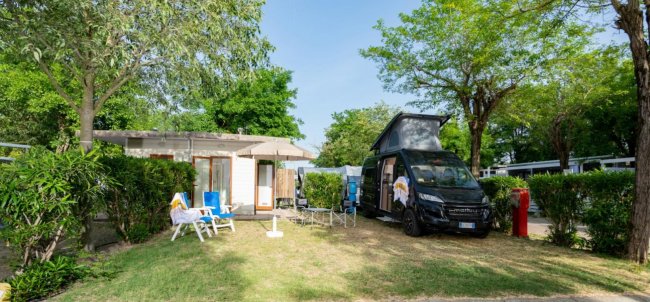 Camper e sedie fuori da una casetta in un campeggio verde.