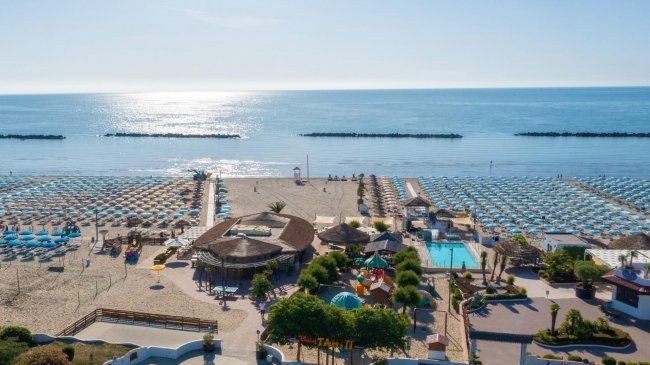 Vista aerea di una spiaggia attrezzata e piscina vicino al mare.