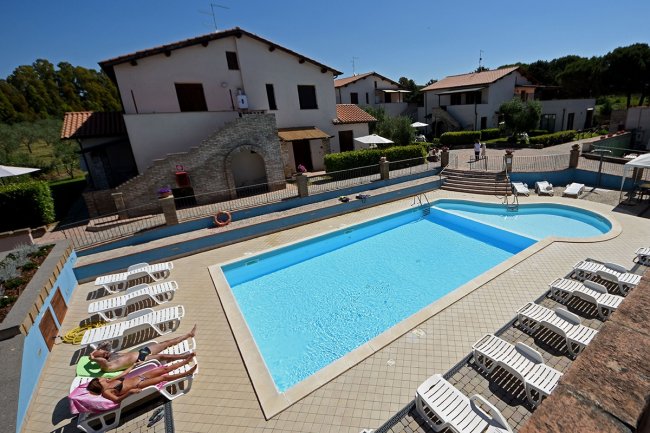 Piscina con lettini e villette in sfondo.