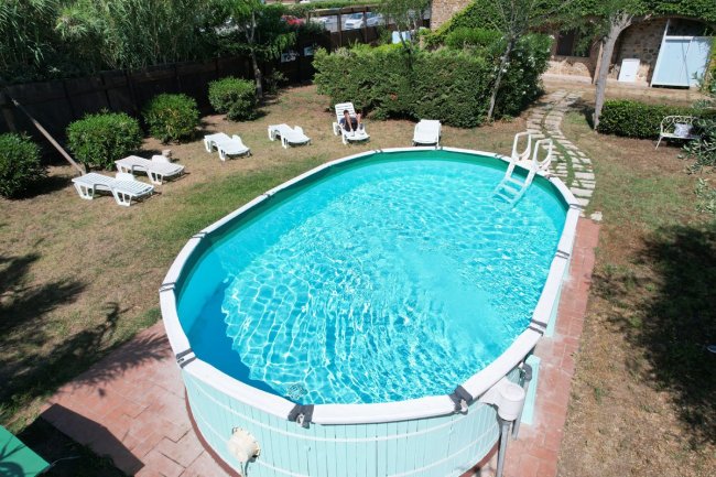 Piscina ovale con lettini bianchi intorno.
