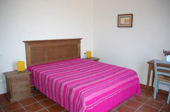 Camera con letto matrimoniale coperto da un copriletto rosa e mobili in legno.