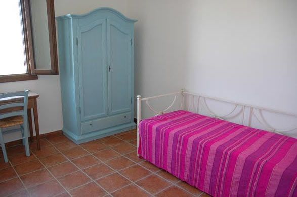 Camera con armadio azzurro, letto singolo con copriletto rosa e una piccola scrivania.