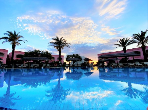 Piscina con palme al tramonto e cielo colorato.
