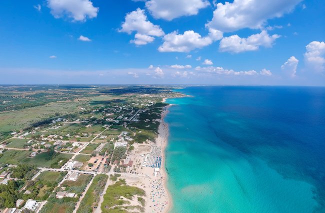 Spiaggia con mare turchese e case lungo la costa.