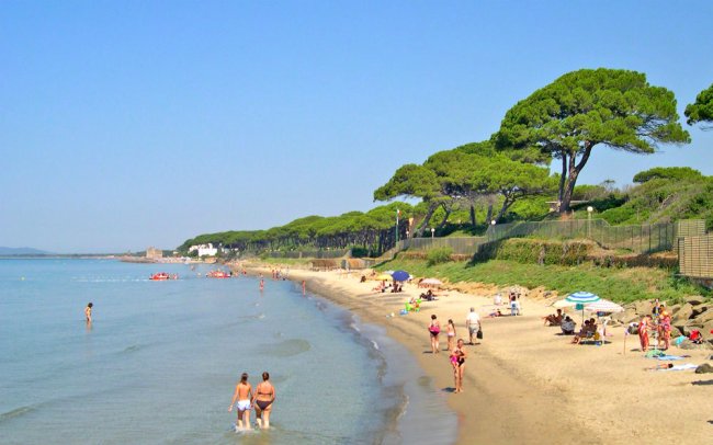 Spiaggia con bagnanti, ombrelloni e mare calmo. Alberi verdi lungo la costa.