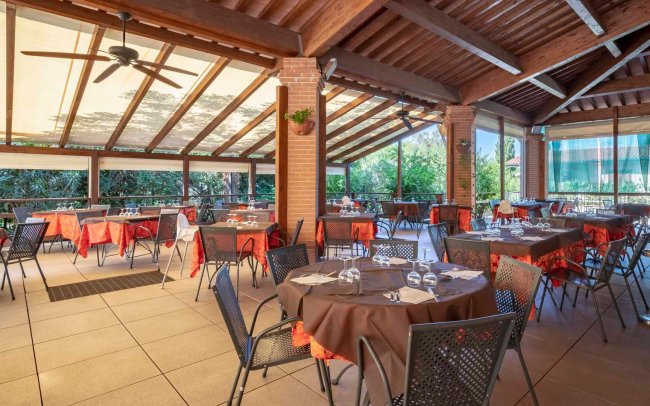 Ristorante all'aperto con soffitto in legno, tavoli apparecchiati e vista sulla vegetazione.