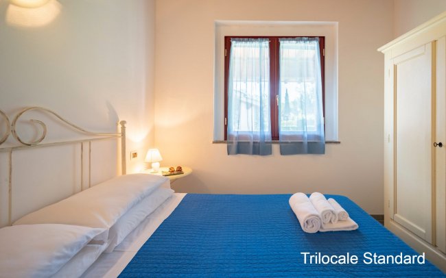Camera con letto matrimoniale, copriletto blu, asciugamani piegati e finestra con tende.