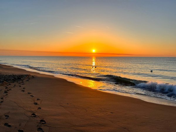 Una spiaggia al tramonto con un cielo arancione e mare calmo.