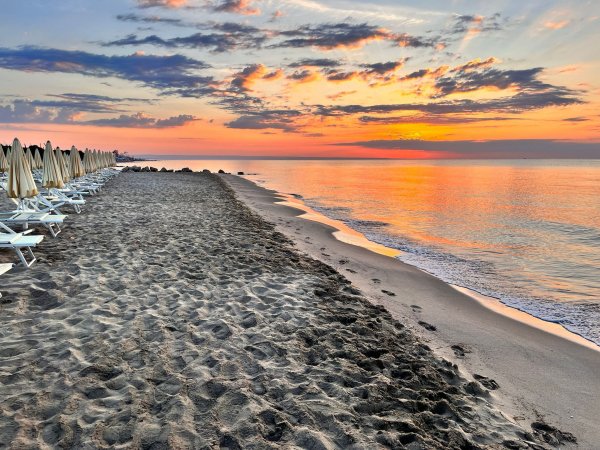 Una spiaggia con lettini vuoti al tramonto e cielo variopinto.