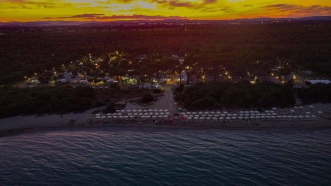 Spiaggia al tramonto con ombrelloni visti dall'alto.