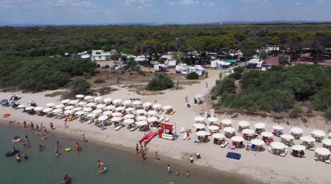 Vista aerea di una spiaggia affollata con ombrelloni e persone che nuotano.