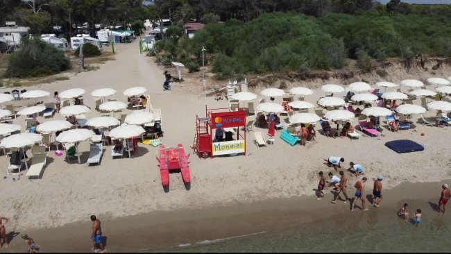 Spiaggia con ombrelloni e lettini, bagnanti e una torre di salvataggio.