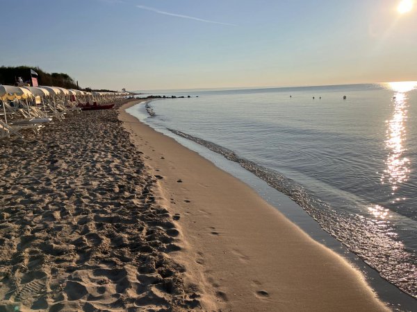 Una spiaggia al tramonto con mare calmo, sdraio bianche e un cielo limpido.