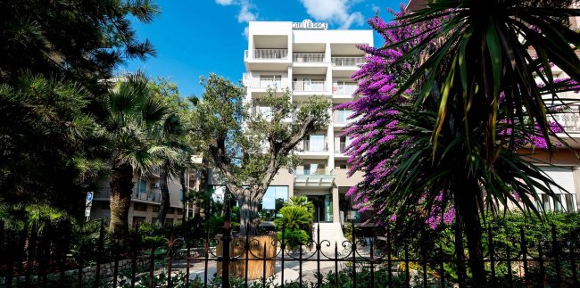 Facciata di un hotel tra alberi e fiori.