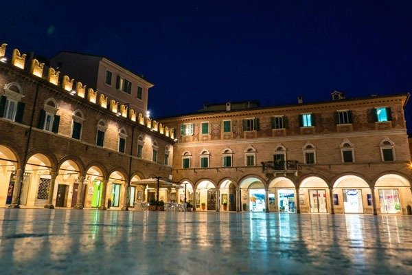Piazza illuminata di notte con edifici storici.
