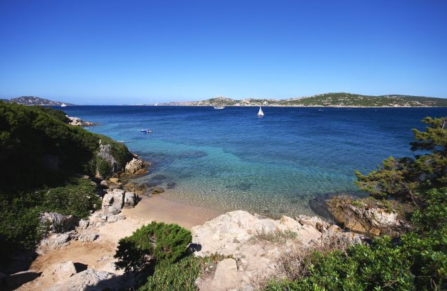 Costa rocciosa con mare blu e una barca a vela.