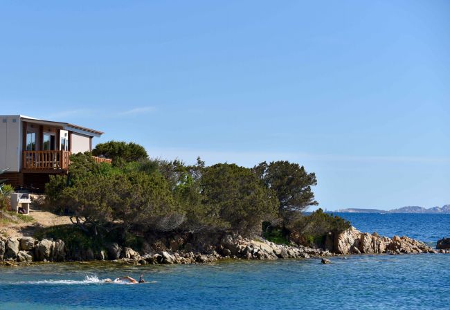 Casetta e nuotatori vicino a un mare blu e rocce.