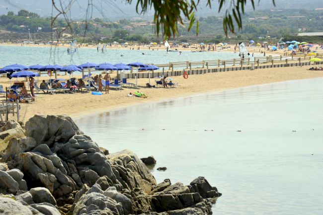 Spiaggia sabbiosa con ombrelloni blu e rocce.