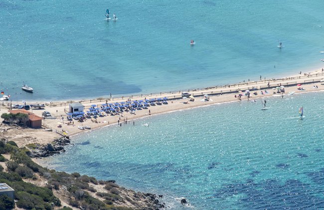 Spiaggia con ombrelloni blu, bagnanti e sport acquatici.