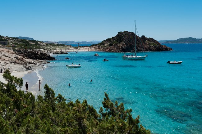 Un'isola con mare turchese e barche a vela.