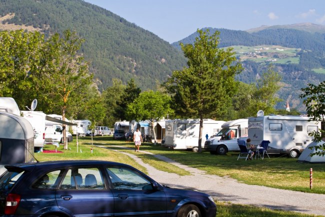 Auto e roulotte in un campeggio montano soleggiato.