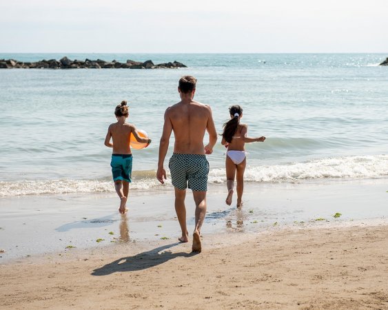 Persone camminano verso il mare su una spiaggia sabbiosa.