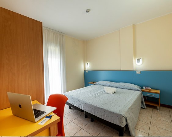 Camera da letto con scrivania, laptop e letto matrimoniale.