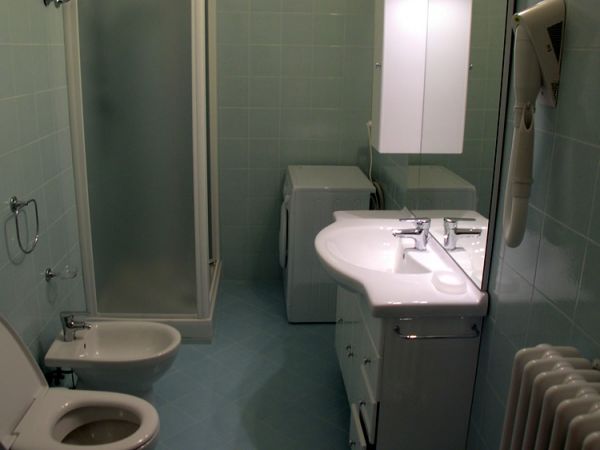 Bagno moderno con doccia, bidet, lavandino doppio e lavatrice. Pareti con piastrelle verdi.