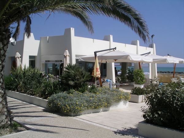 Edificio bianco moderno con terrazza, circondato da piante e affacciato sul mare.