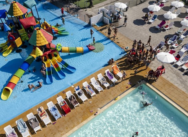 Piscina con area giochi colorata e lettini bianchi.