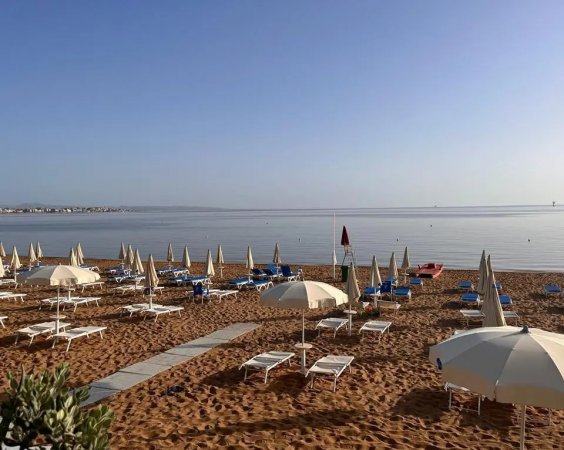 Spiaggia sabbiosa con ombrelloni e lettini, mare calmo sullo sfondo.