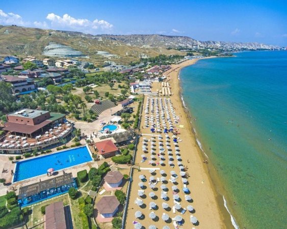 Vista aerea di una spiaggia con ombrelloni e un resort con piscina.