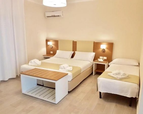 Camera con letto matrimoniale e singolo, due lampade e tavolino. Asciugamani piegati sui letti.